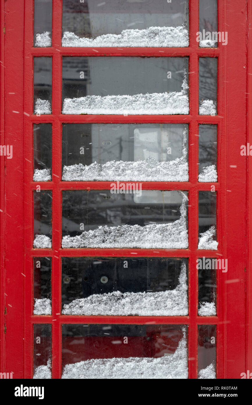 Rote Telefonzelle in Winson Dorf im Winter Schnee. Winson, Cotswolds, Gloucestershire, England Stockfoto