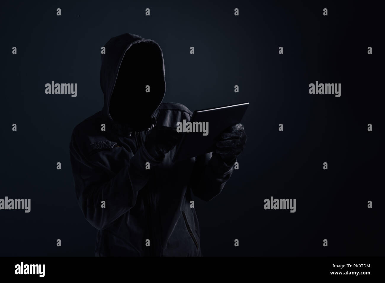 Hooded computer Hacker mit Verwendung der digitalen tablet Cyberkriminalität und Cybersicherheit Konzept verdeckt Gesicht, Low Key mit selektiven Fokus Stockfoto