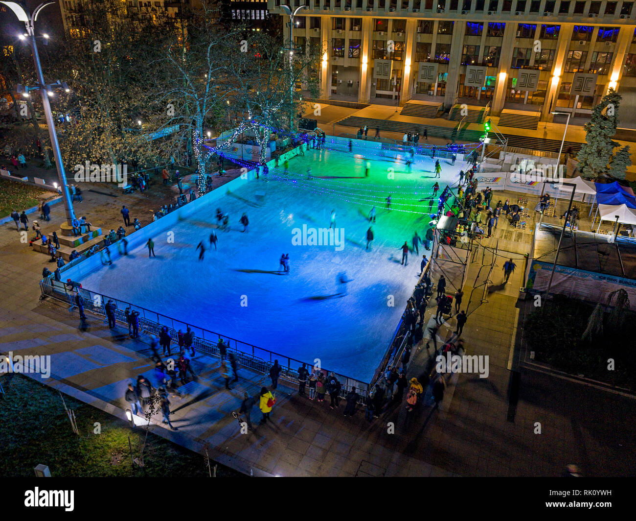 Drone Ansicht von oben. Viele Menschen sind Eislaufen in der Eissporthalle in 'Troikata" Platz am Abend, Luftbild. Stockfoto