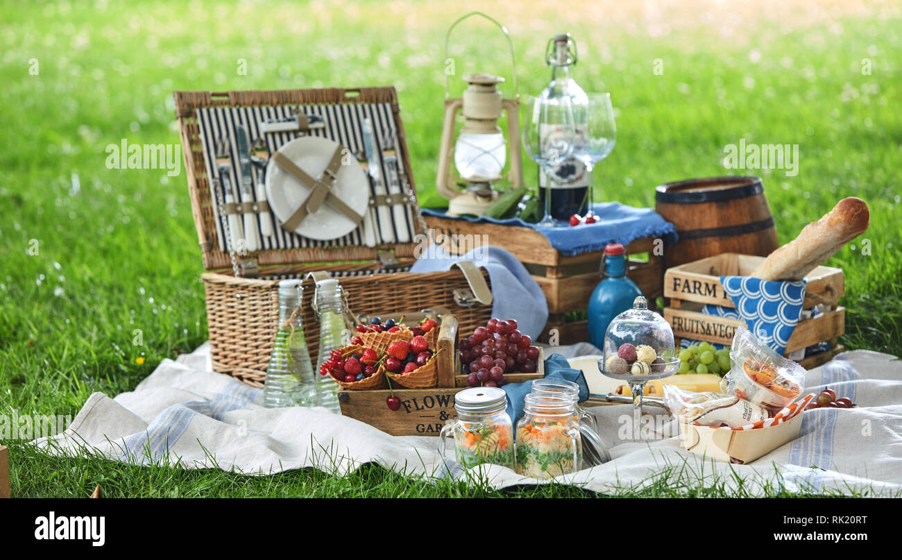 Vintage Style Picknick mit Mittagessen im Park auf einer Decke auf dem Rasen mit Käse behindern, frisches Obst, Bonbons, Pickles Brot und Rotwein Stockfoto