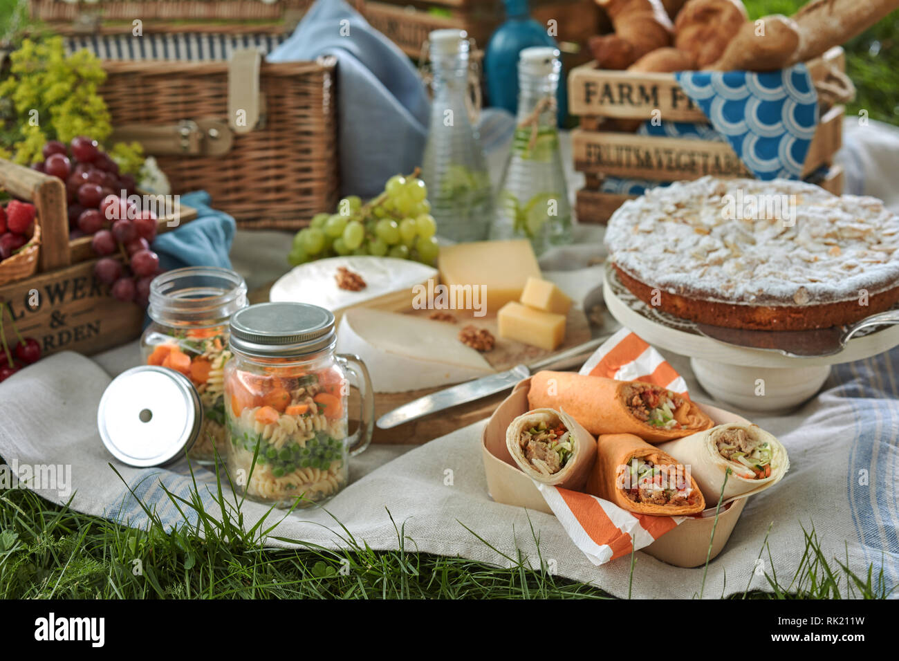 Picknick auf einer Decke auf dem Rasen mit Gemüse Konserven, Veggie Wraps, Käse, Weintrauben, Kuchen zum Nachtisch und kalten Wasser hineingegossen in Bot Stockfoto