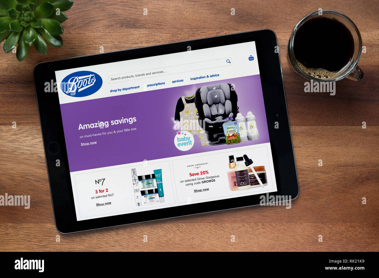 Die Website der Stiefel ist auf einem iPad Tablet gesehen, auf einer hölzernen Tisch zusammen mit einem Espresso und einem Haus Anlage (nur redaktionelle Nutzung). Stockfoto