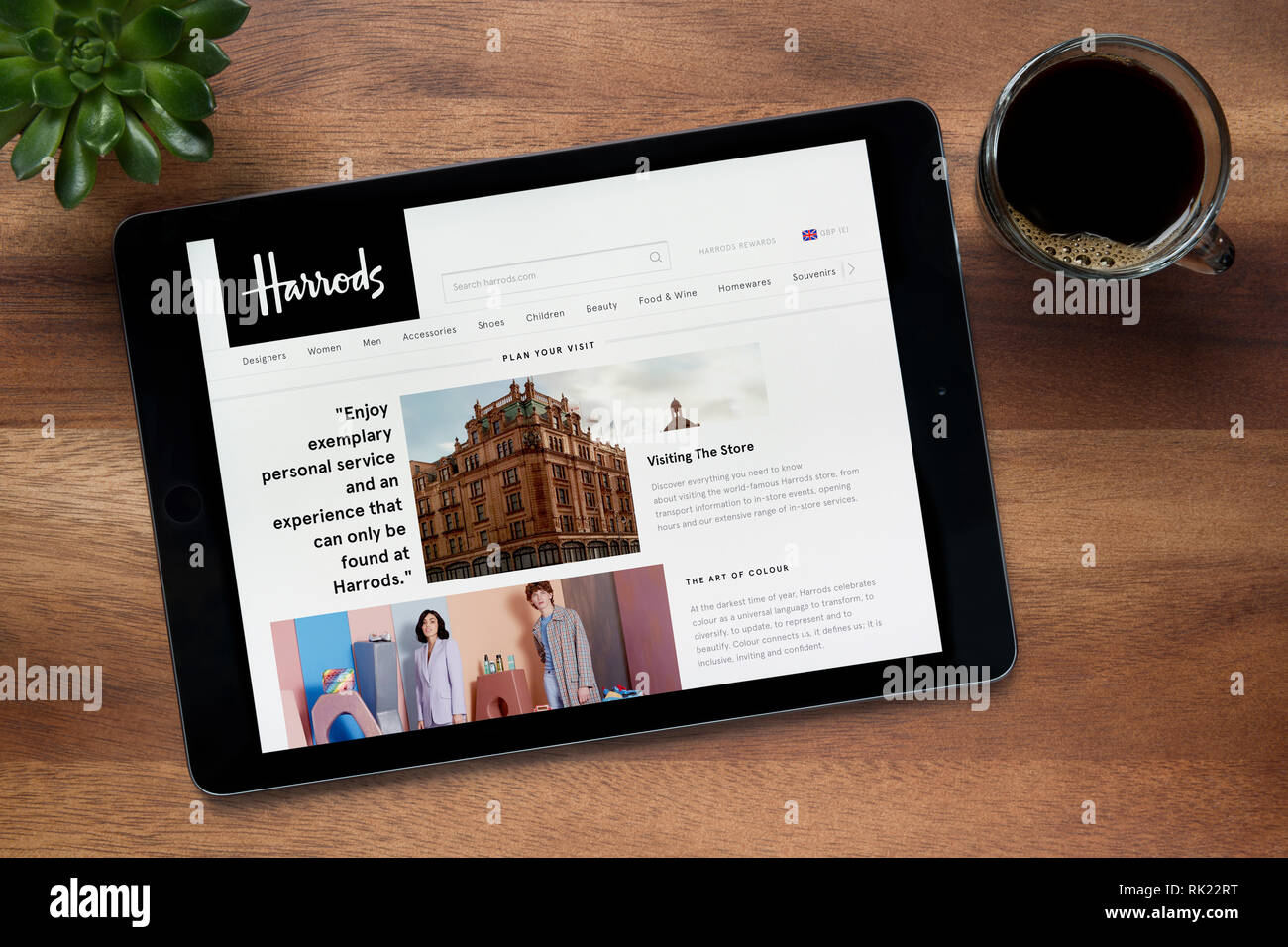 Die Website von Harrods ist auf einem iPad Tablet gesehen, auf einer hölzernen Tisch zusammen mit einem Espresso und einem Haus Anlage (nur redaktionelle Nutzung). Stockfoto