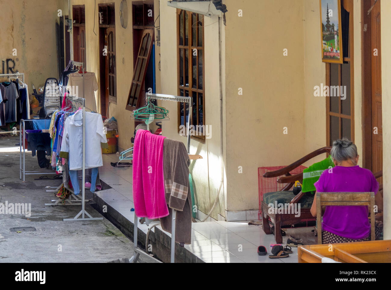 Dame auf der Veranda von Regalen gebügelte Kleidung und Handtücher, Jimbaran, Bali Indonesien umgeben. Stockfoto