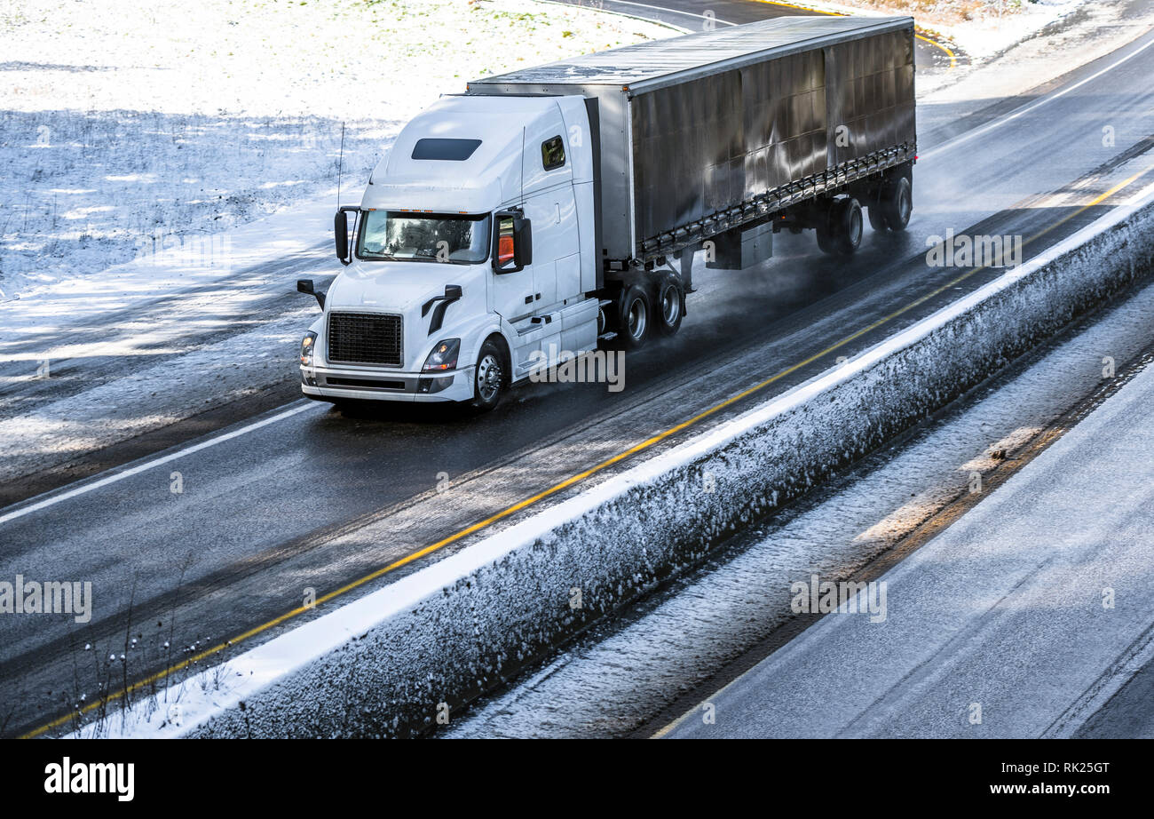 Big Rig Long Haul grau Semi Truck Traktor Transport von kommerziellen Ladung in trockenen van Auflieger gehen auf den nassen rutschigen Straße mit Wasser aus Schmelzen Stockfoto