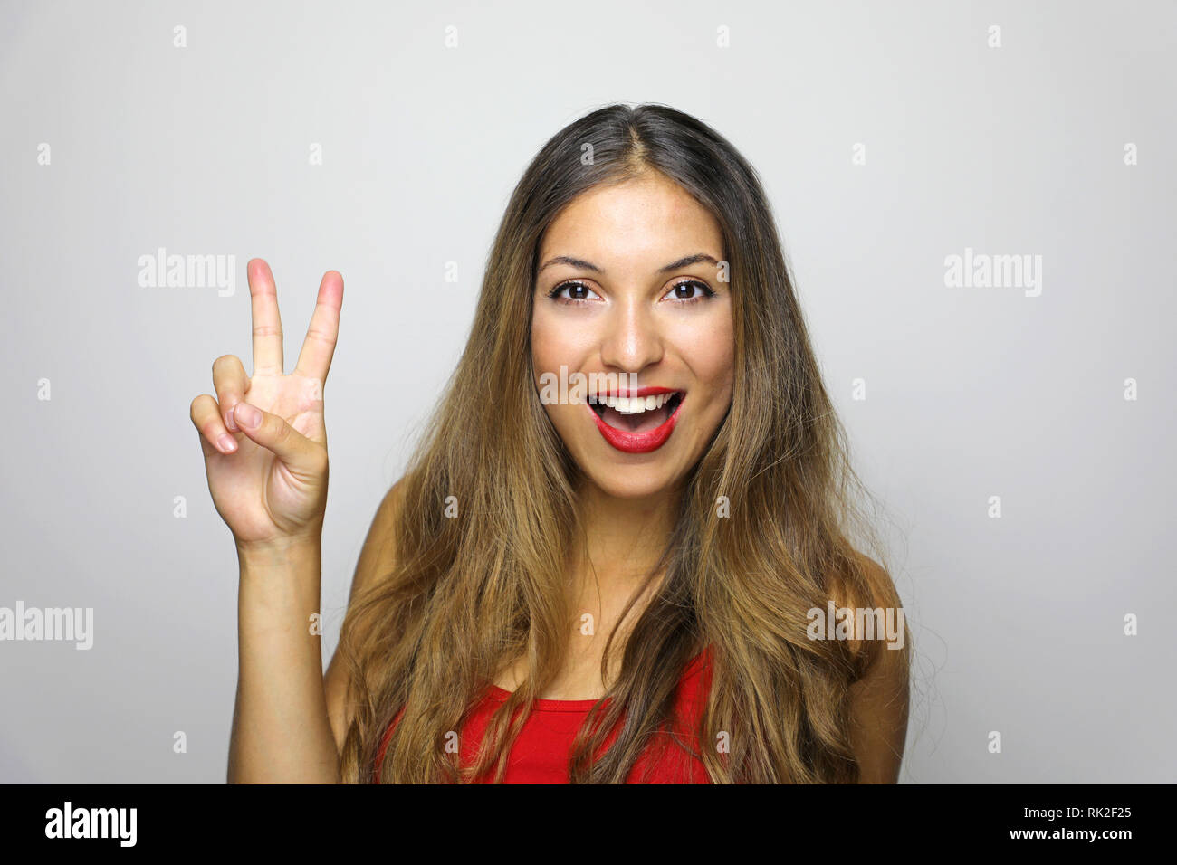 Portrait von lächelnden Frau, Sieg Schild mit roter Tank Top, und wenn man die Kamera auf dem grauen Hintergrund isoliert Stockfoto