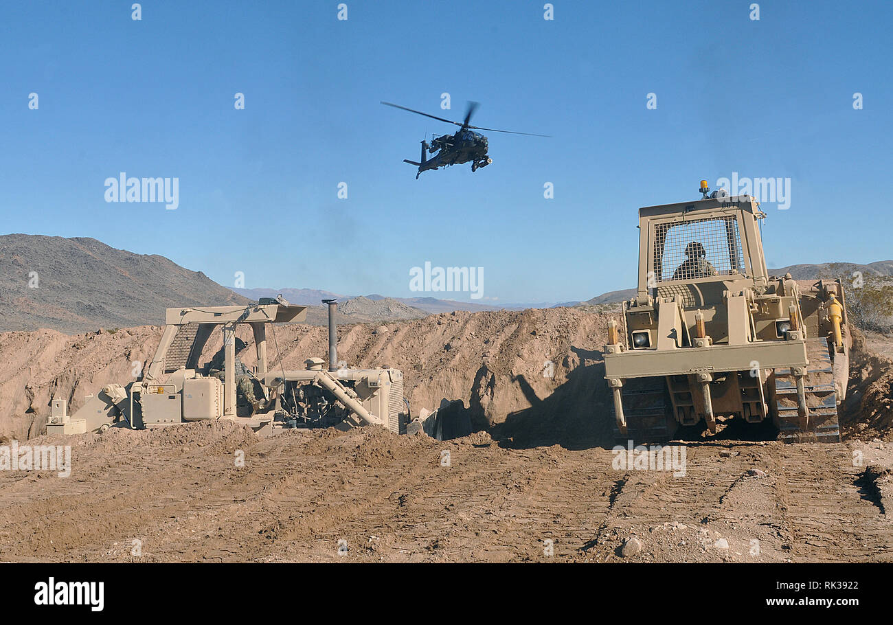 Ein U.S. Army Apache Kampfhubschrauber seaarches Für entgegengesetzte Kräfte oder AUFSTÄNDISCHE, als es über US Army Reserve Soldaten in der 718Th Engineer Company, Engineer Battalion, 926Th Engineer Brigade, 412 Theater Ingenieur Befehl in Fort Benning, Ga basierend Fliegen, mit Ihrer D7G Bulldozer um eine Anti-Fahrzeug graben während der Rotation 19-03 am National Training Center auf Fort Irwin, Calif., Jan. 18, 2019 dig. (U.S. Armee finden Foto von Sgt. 1. Klasse Clinton Holz). Stockfoto