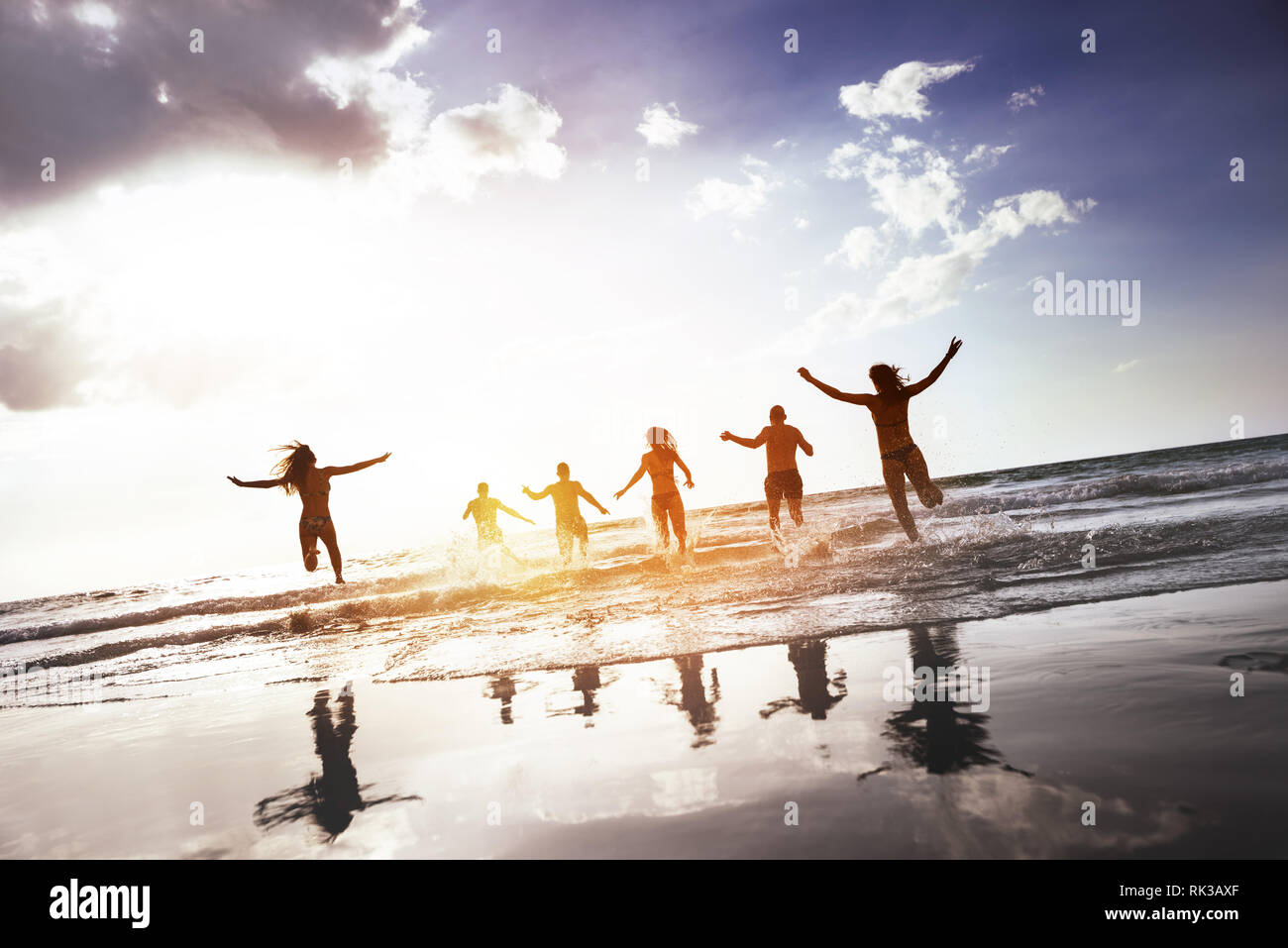 Gruppe der glücklichen Völker läuft und springt bei Sonnenuntergang am Strand. Tropische Tourismus Konzept Stockfoto