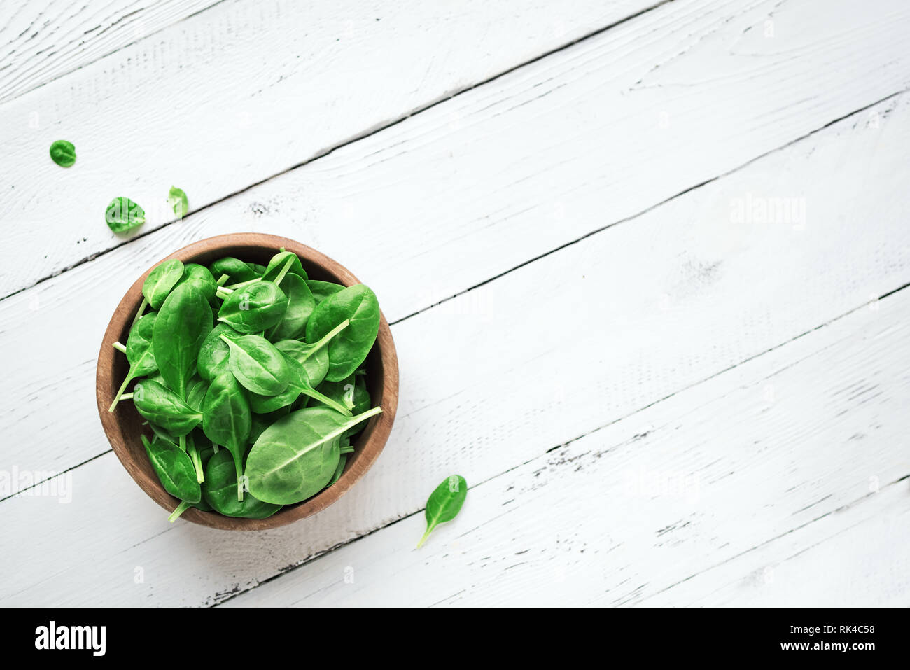 Baby Spinatblätter in der Schüssel auf weißem Holz- Hintergrund, Ansicht von oben, kopieren. Sauber Essen, Detox, Diät Lebensmittel Zutat - grün Bio Spinat. Stockfoto