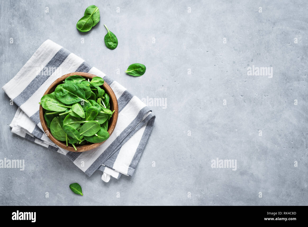Baby Spinatblätter in Schüssel auf grauem Beton Hintergrund, Ansicht von oben, kopieren. Sauber Essen, Detox, Diät Lebensmittel Zutat - grün Bio Spinat. Stockfoto