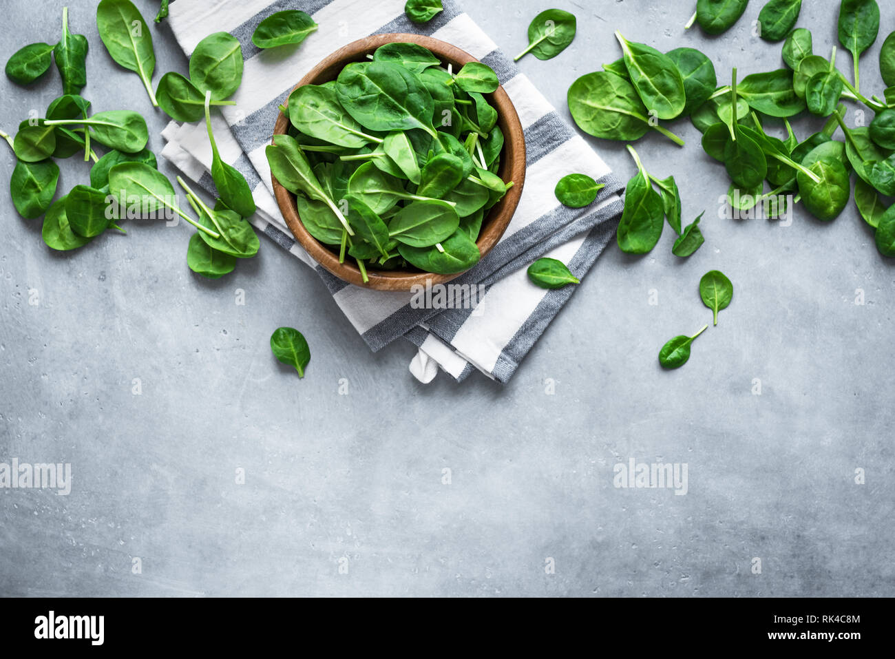 Baby Spinatblätter in Schüssel auf grauem Beton Hintergrund, Ansicht von oben, kopieren. Sauber Essen, Detox, Diät Lebensmittel Zutat - grün Bio Spinat. Stockfoto