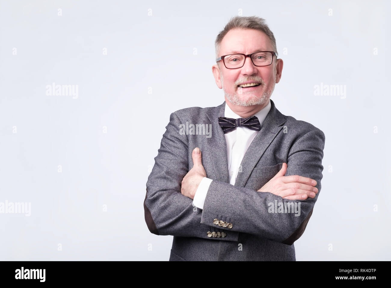 Senior Geschäftsmann in Anzug und Fliege mit verschränkten Armen posing Stockfoto
