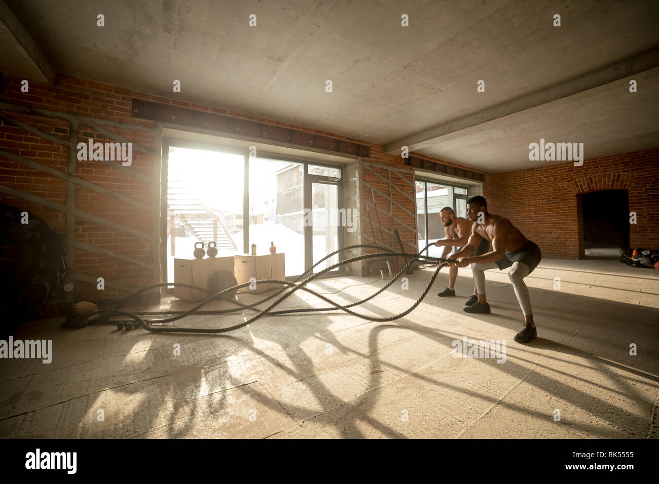 Zwei multiethnischen shirtless männlichen Bodybuilder Trainieren mit Seile kämpft. Die hohe Intensität und schnelle Art der Ausbildung mit einem Seil wird. Stockfoto