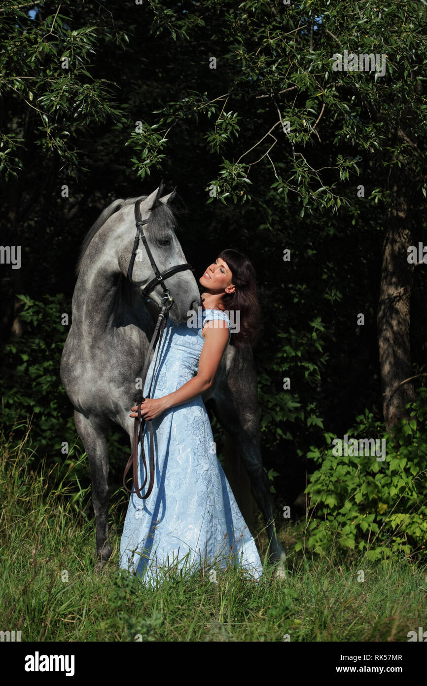 Schöne brünette Frau mit langen Haaren und blauen Kleid in den Wäldern mit dapple graues Pferd Stockfoto
