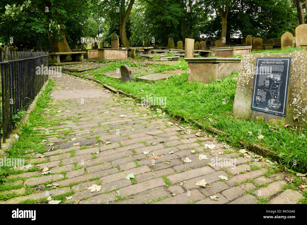 Kopfsteinpflastereingang des Friedhofs, Touristeninformationstafel, Grabsteine und Denkmäler - St. Michael & All Angels Church, Haworth, West Yorkshire, England, Großbritannien. Stockfoto