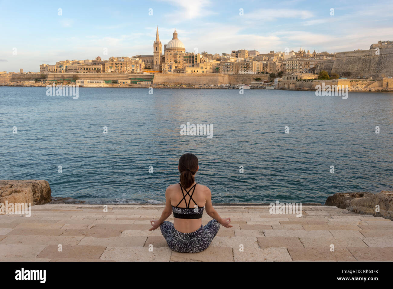 Rückansicht einer Frau, meditieren, Yoga mit Valletta, Malta als Hintergrund Stockfoto