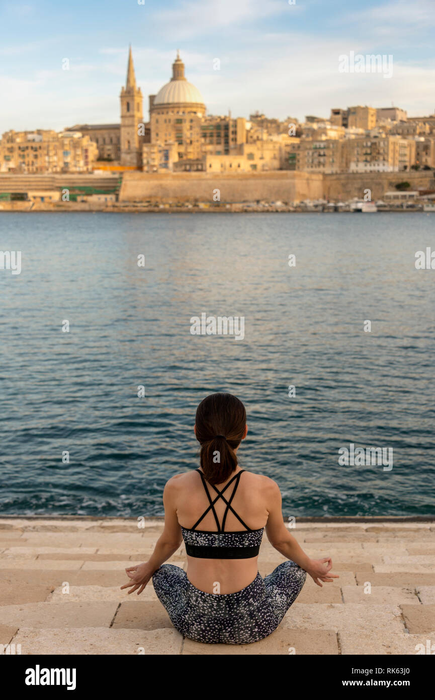 Rückansicht einer Frau, meditieren, Yoga mit Valletta, Malta als Hintergrund Stockfoto