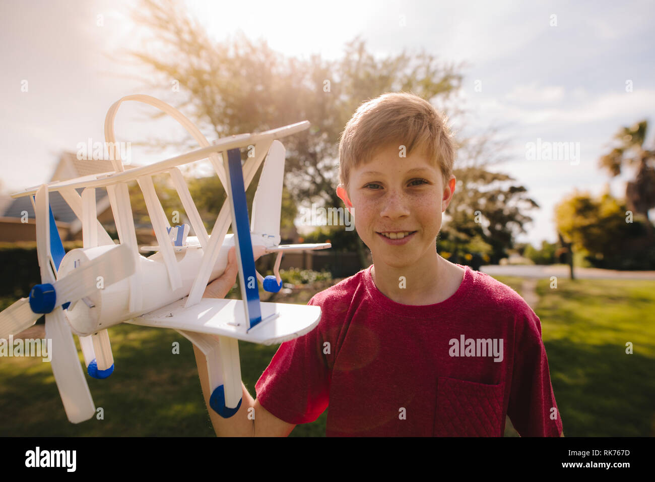 Glückliche junge Junge mit einem Flugzeug im Freien an Kamera schaut. Jugendliche Junge spielt mit seinem Spielzeug Flugzeug. Stockfoto