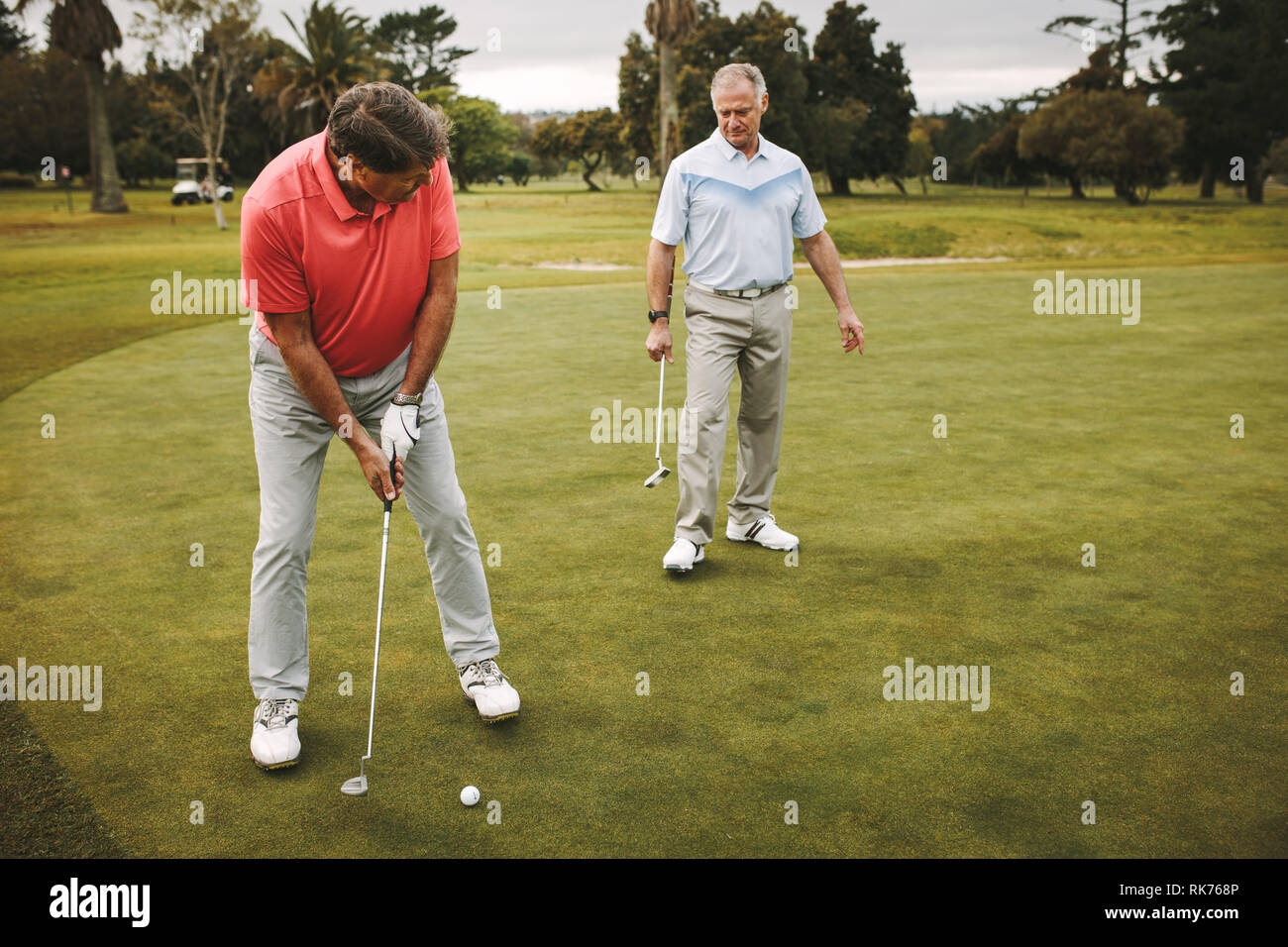 Ältere Golfspieler auf putting green Über den Schuß zu nehmen. Männliche Golf Spieler setzen auf Grün mit zweiten Spieler, der an der Rückseite. Stockfoto