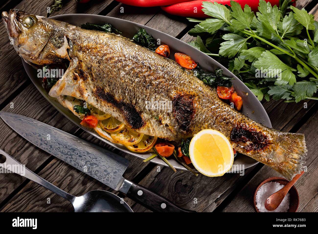 Schöner ganzer Fisch gegrillt und serviert auf einer Metallpfanne mit Tomaten, Zitrone und Kräutern Stockfoto