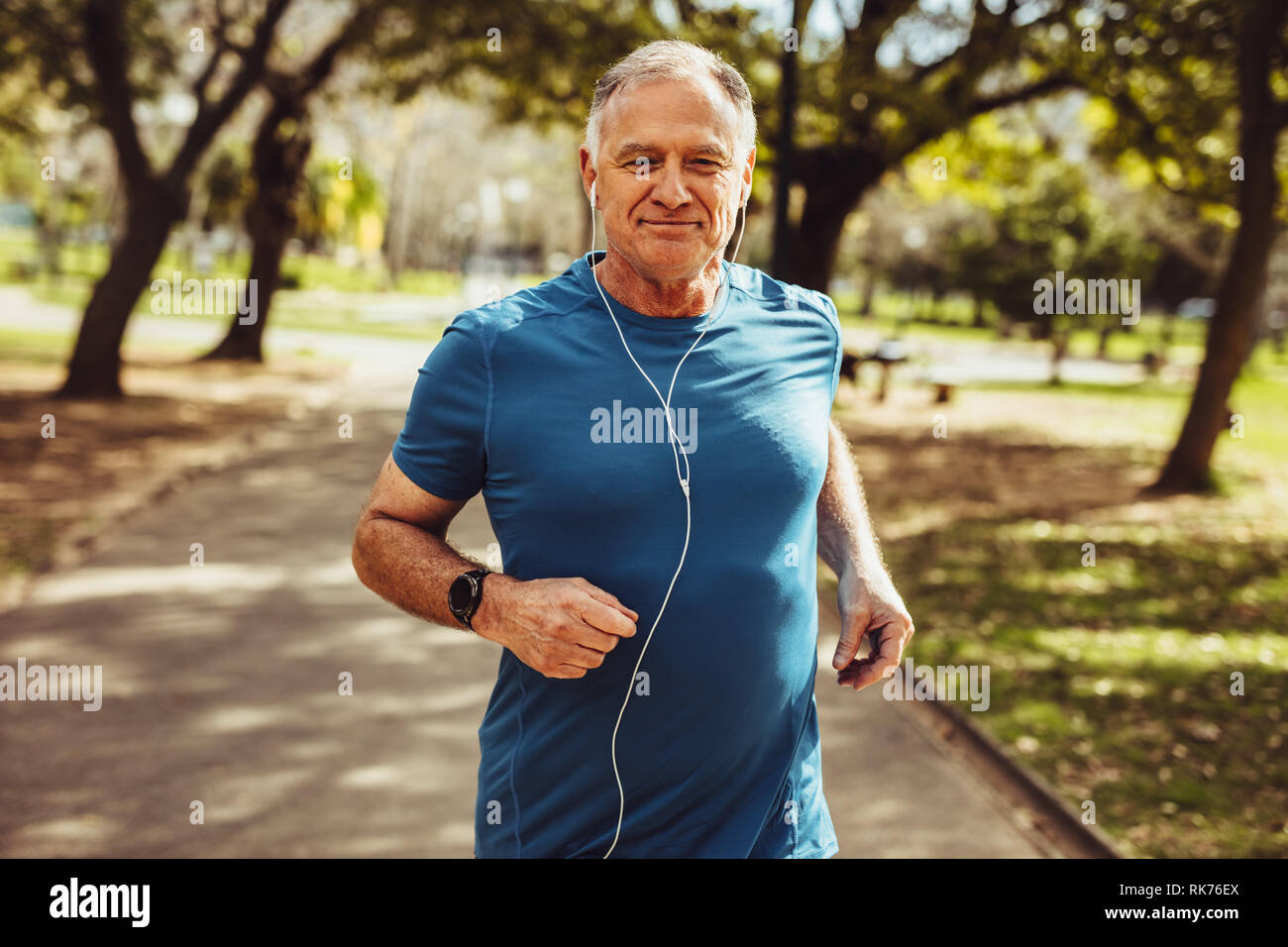Fröhlicher älterer Mann Joggen im Park das Hören von Musik über Kopfhörer. Senior Fitness person im Park für eine gute Gesundheit. Stockfoto