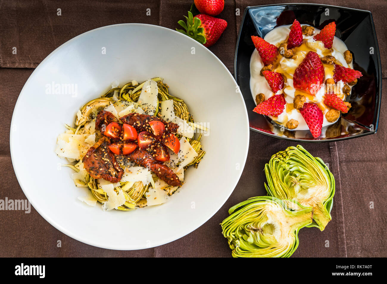 Nahaufnahme von einem Bogen von frischen Artischocken Salat mit roten Tomaten Cherry und Parmesan und einem Bogen leckeren Joghurt mit frischen roten Erdbeeren Stockfoto