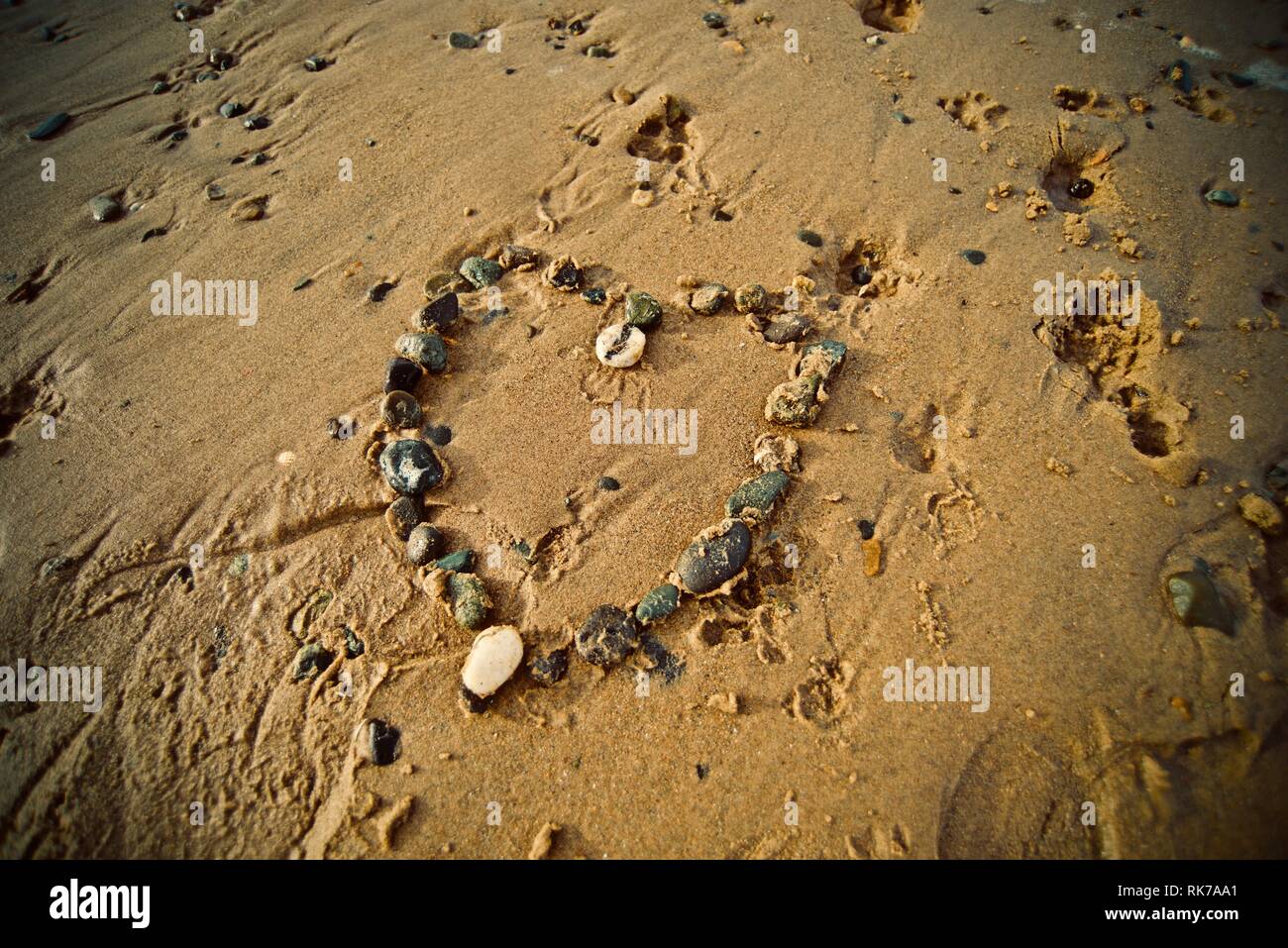 Ein Herz aus Steinen auf dem Sand des Strandes mit der Tide, die hereinkommen, Rhosneigr, Anglesey, North Wales, UK Stockfoto