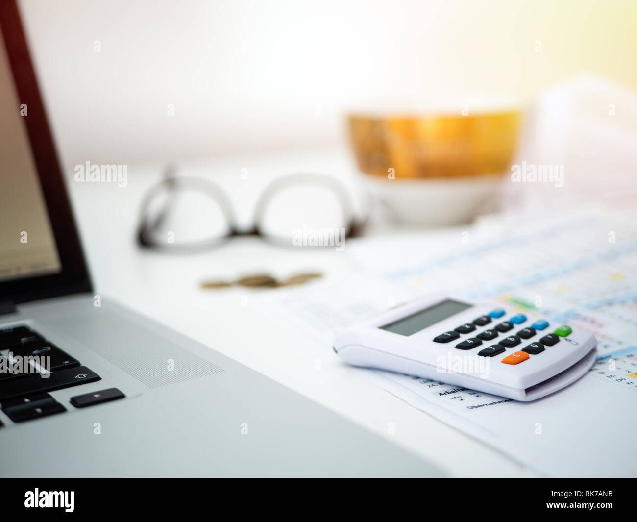 Home Office: Schreibtisch mit Laptop, Rechner und andere Büroartikel. Kaffee Becher und Gläser im Hintergrund Stockfoto