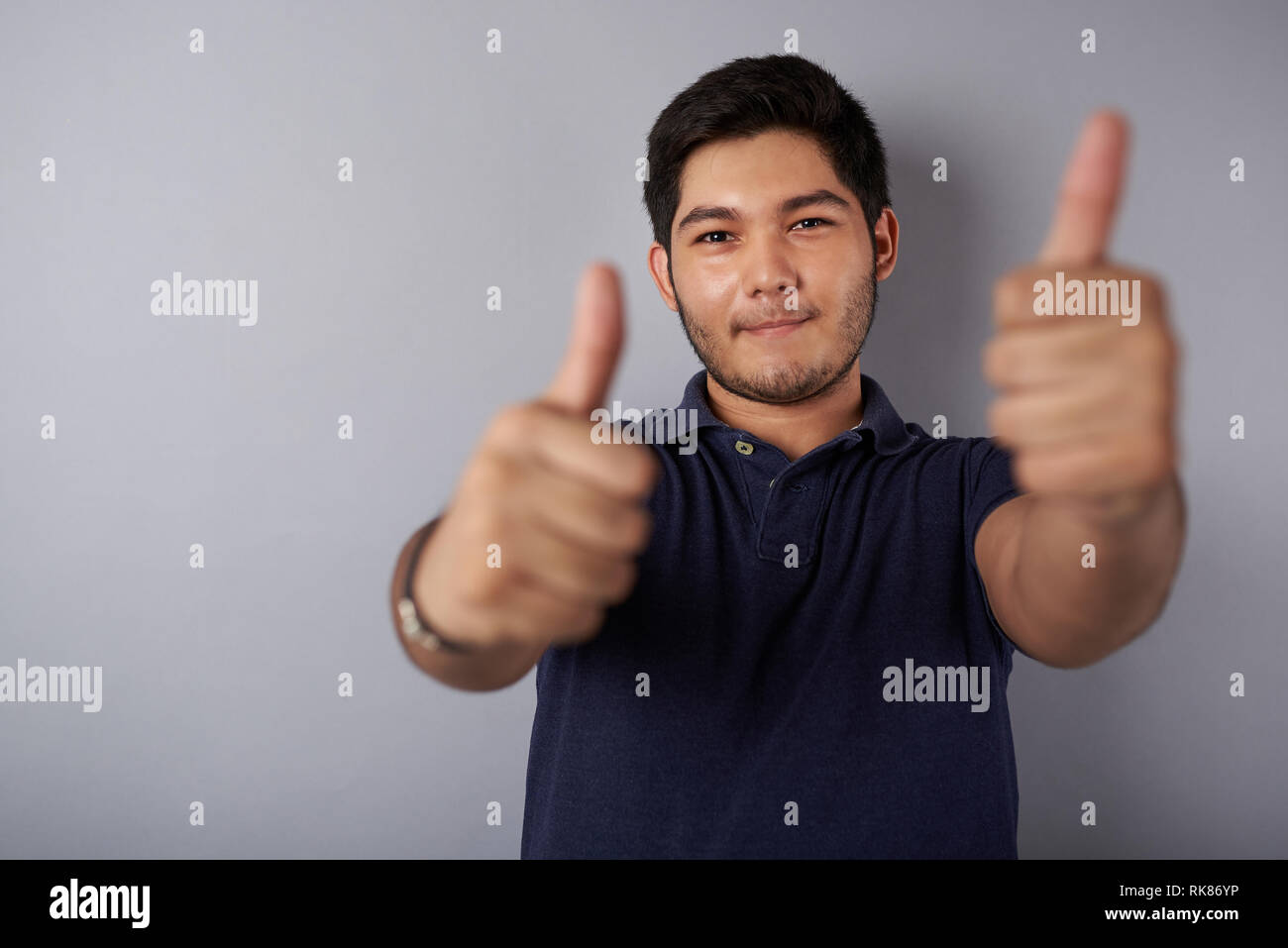 Teenager zeigen Daumen hoch auf grauem Hintergrund Stockfoto