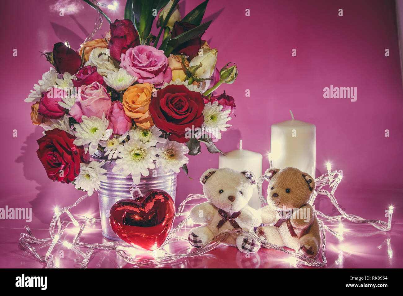 Vase Bouquet Rosen in Aluminium Schaufel und Rot funkelnden Herzen. Paar schöne Bären sitzen in der Nähe von white Kerzenständer auf rosa Hintergrund. Leuchten Licht Stockfoto