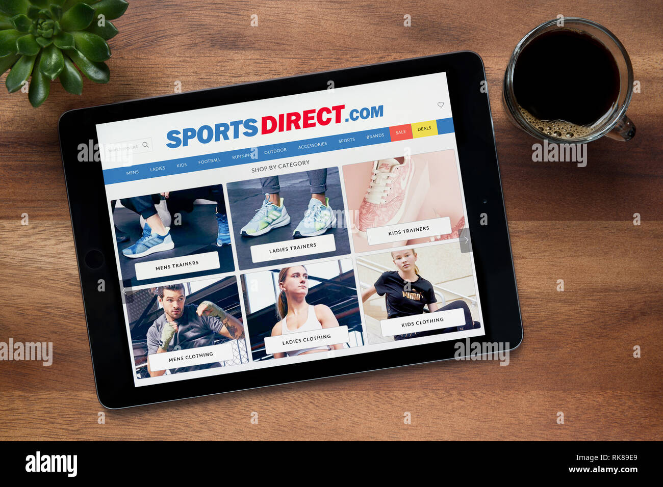 Die Website von Sport Direct ist auf einem iPad Tablet gesehen, auf einer hölzernen Tisch zusammen mit einem Espresso und einem Haus Anlage (nur redaktionelle Nutzung). Stockfoto