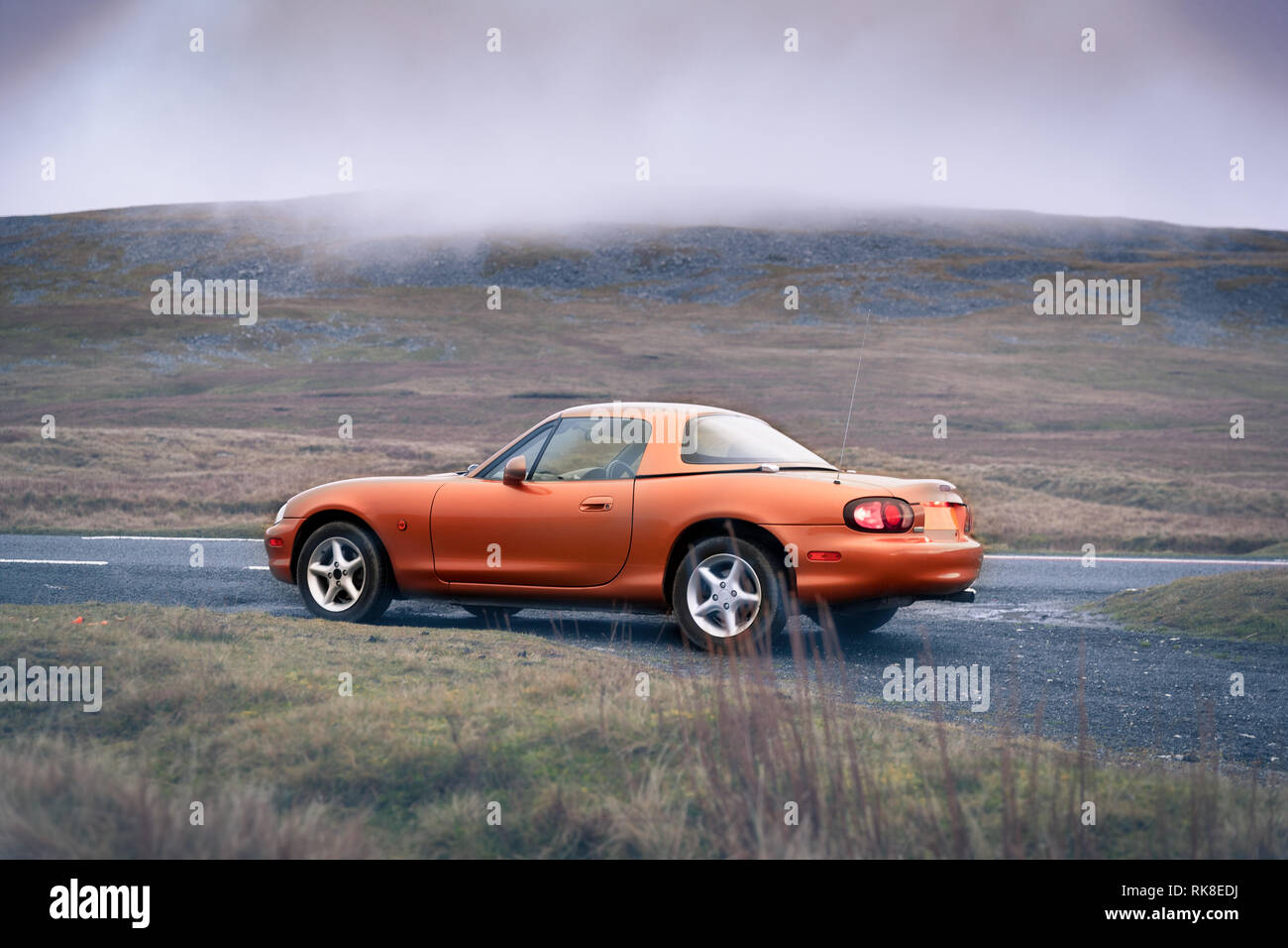 Sportlich wenig Gold Coupé mit Hardtop auf der Straße geparkt werden. Ein Welsh Mountain auf einem grauen englischen Tag in den Wolken. Stockfoto