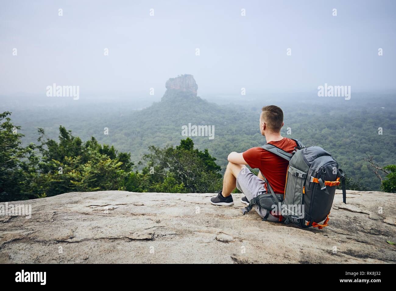 Junger Mann mit Rucksack gegen Sigiriya Felsen (UNESCO-Weltkulturerbe). Blick von pidurangala Felsen in Sri Lanka. Stockfoto
