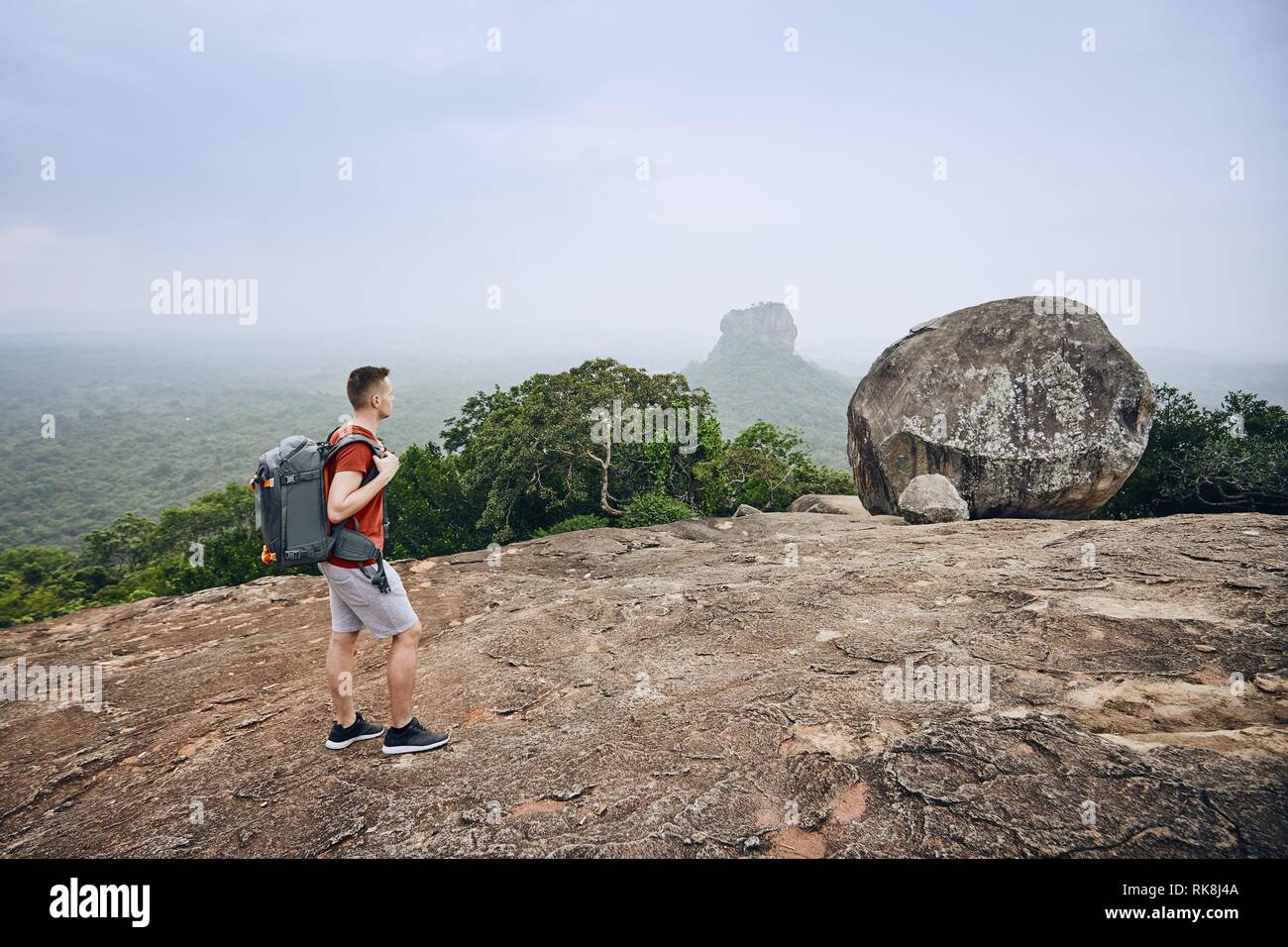 Junger Mann mit Rucksack gegen Sigiriya Felsen (UNESCO-Weltkulturerbe). Blick von pidurangala Felsen in Sri Lanka. Stockfoto