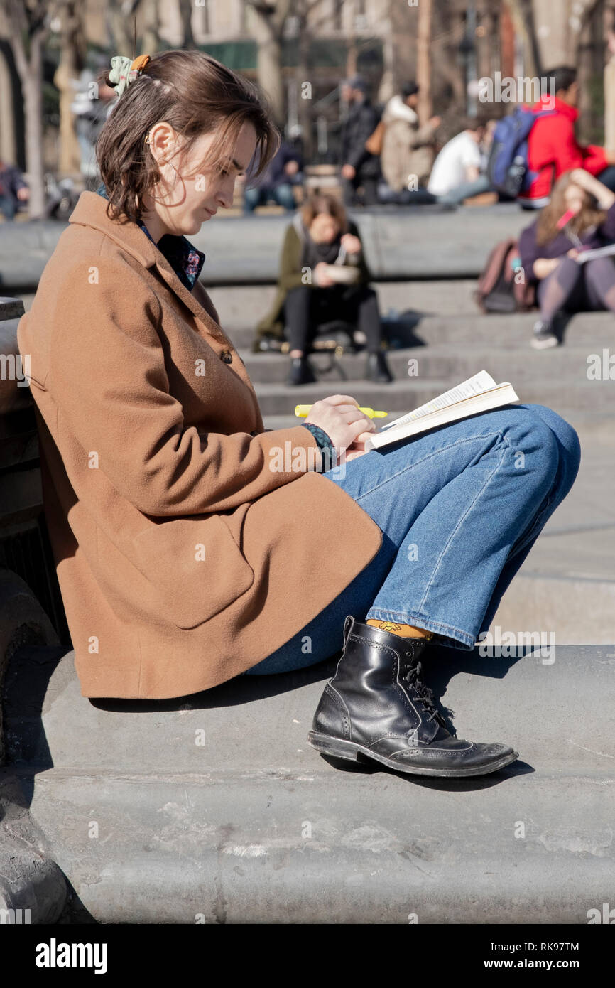 Eine attraktive junge Dame, vermutlich ein Student, liest aus einem Buch und unterstreicht mit einem Magic Marker. Im Washington Square Park in New York City Stockfoto