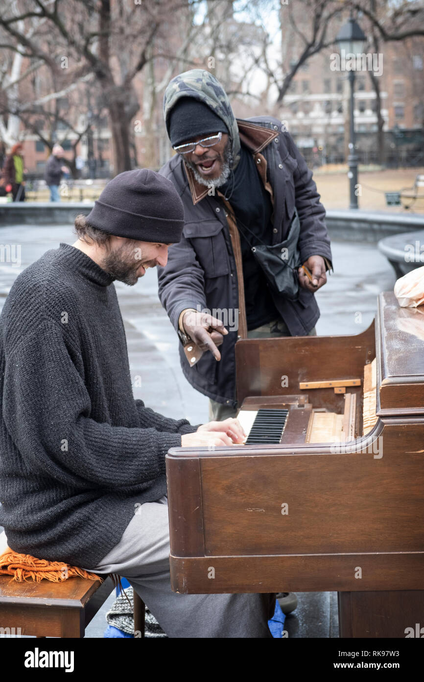 Ein Klavier spielen Gaukler führt mit einem Passanten bye Wer hat blues Duette mit ihm auf seiner Mundharmonika. Im Washington Square Park in Manhattan, New York City. Stockfoto