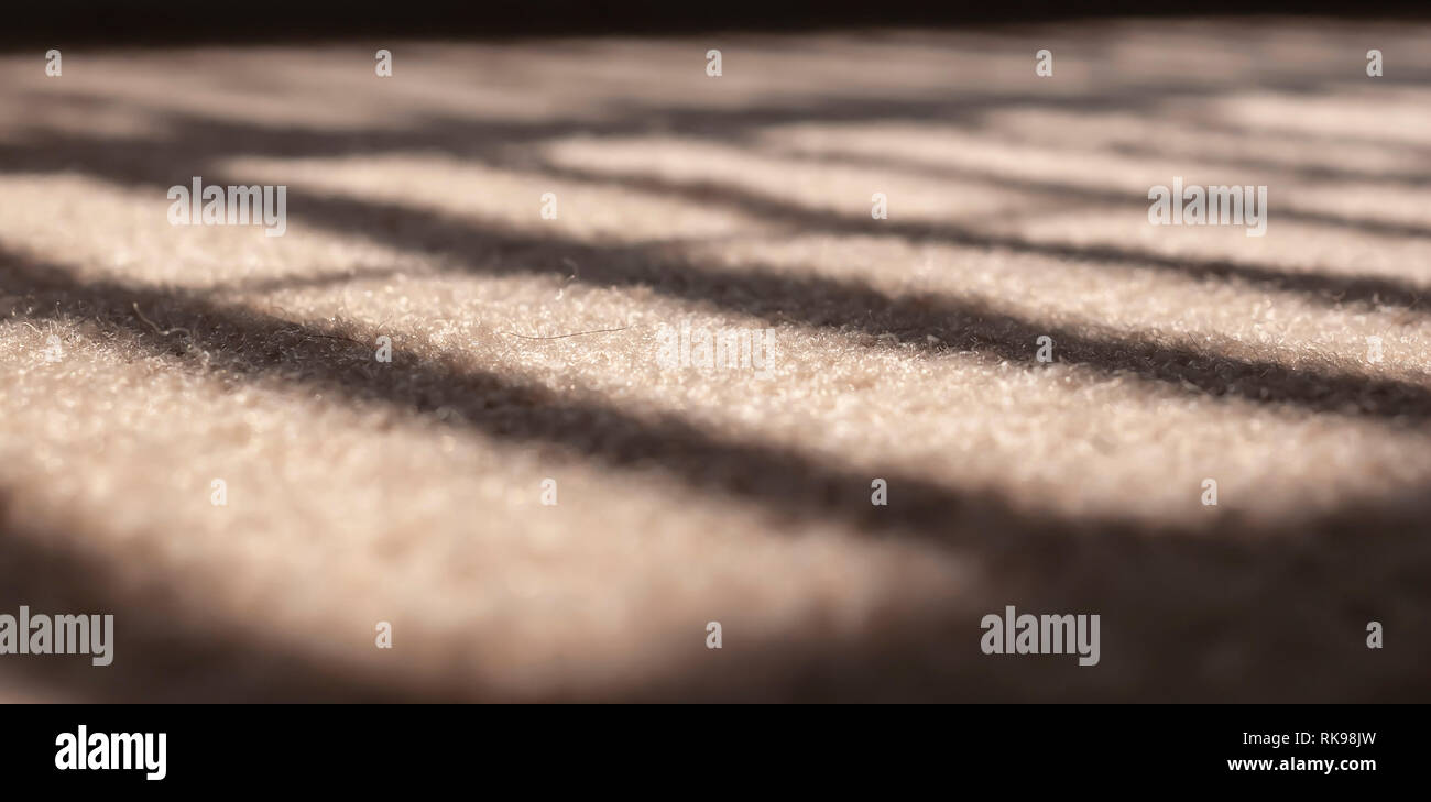 Sonnenlicht Filterung durch Jalousien in einem Fenster Erstellen einer Licht und Schatten Muster auf einem beigen Teppich. Bild mit extrem geringer Tiefenschärfe. Stockfoto