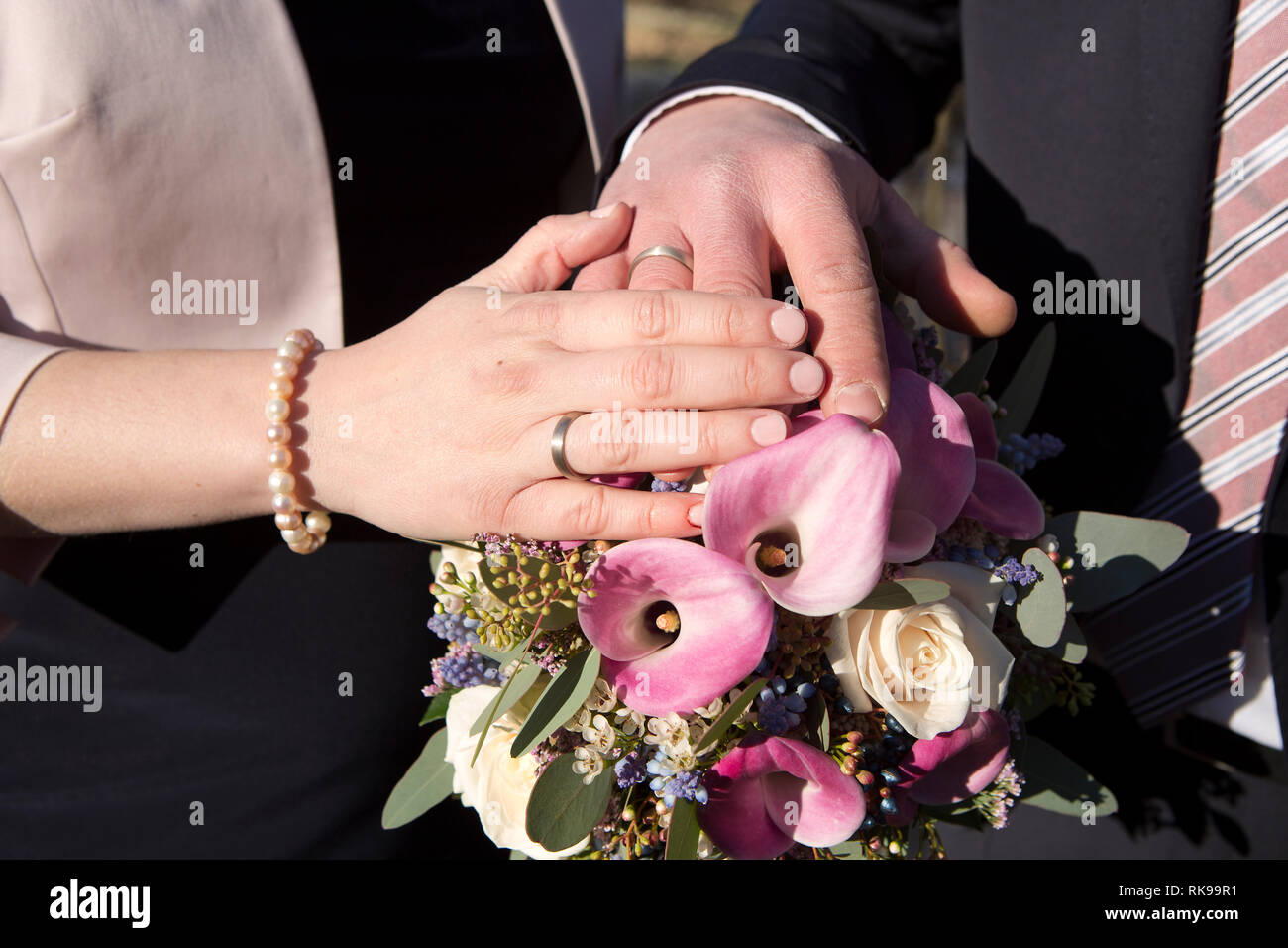 Hände von Braut und Bräutigam mit Blumenstrauß und Trauringe Stockfoto