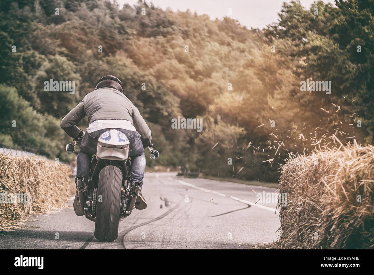 Motorradfahrer sein Fahrrad beschleunigen auf einer geraden Waldweg mit Stücken von Heu Heu Ballen Abblasen ein Stockfoto