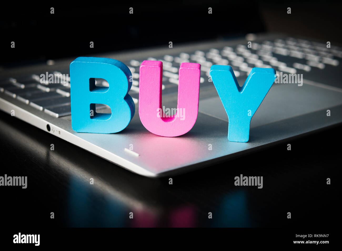 Kaufen Wort auf Laptop unten am schwarzen Hintergrund. Holz- bunte Buchstaben B, U, Y auf geöffnet Notebook gesetzt. Konzept des Kaufens Dinge im Internet. Online sh Stockfoto