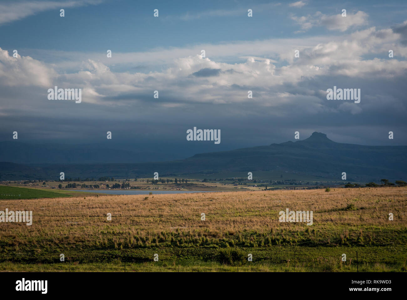 Eine grasbedeckte Ebene und dunstige Berge in der Ferne, bis in den späten Abend Sonne beleuchtet. Drakensberge, Südafrika Stockfoto