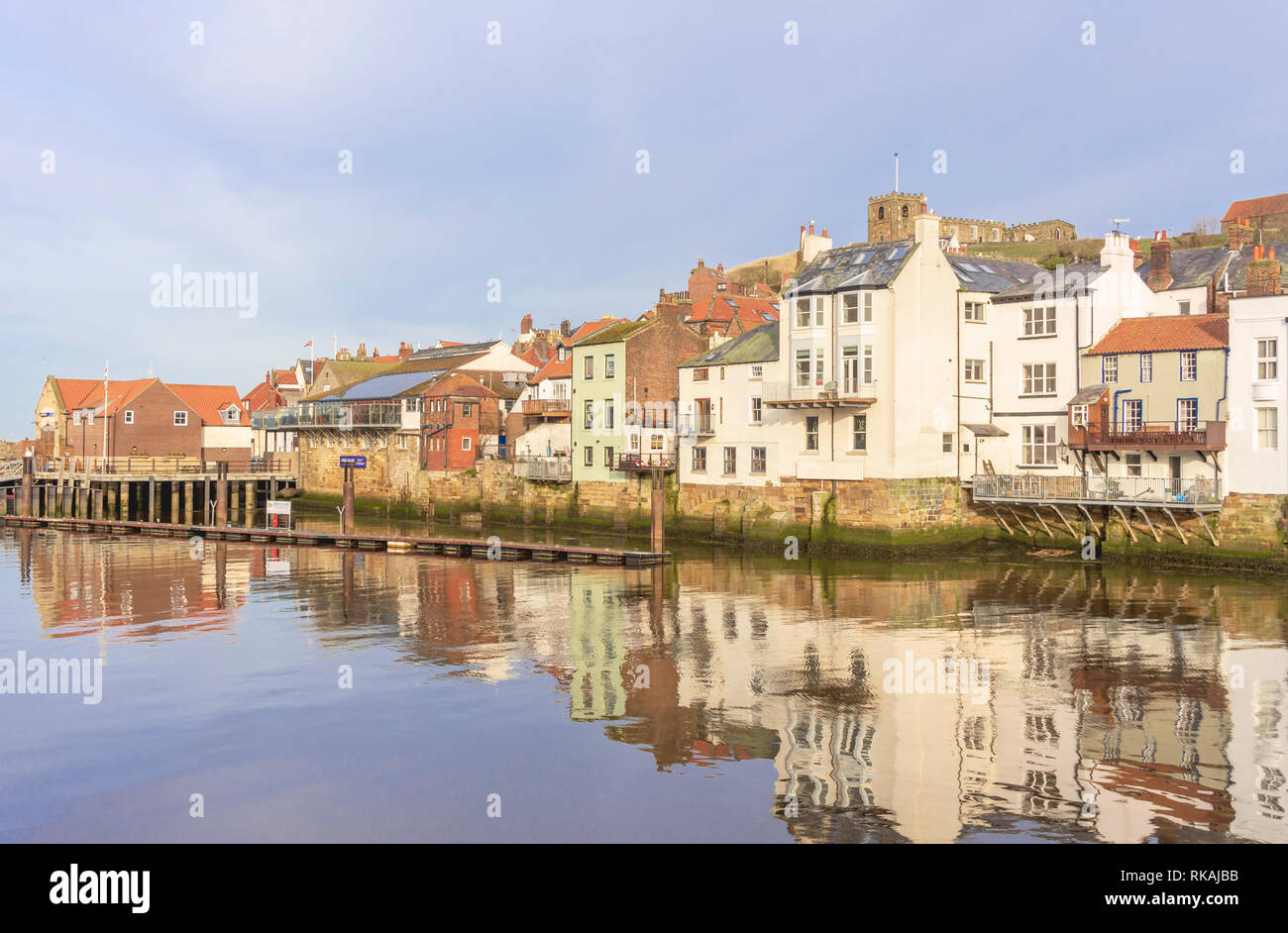 Gebäude entlang der Uferpromenade am Whitby im Wasser des Hafens wider. Einem Hügel überragt die Häuser mit einer Kirche auf dem Gipfel. Stockfoto