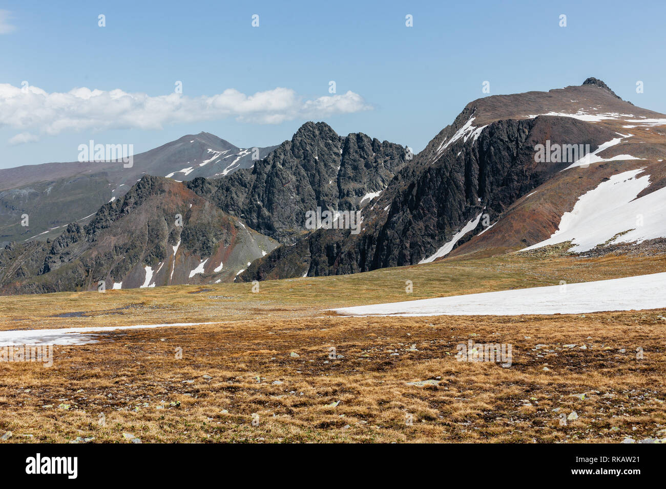 Schöne Aussicht auf die Berghänge bedeckt mit vergilbten Gras und schneebedeckten Gebieten gegen den blauen Himmel und Wolken vorbei. Konzept Stockfoto