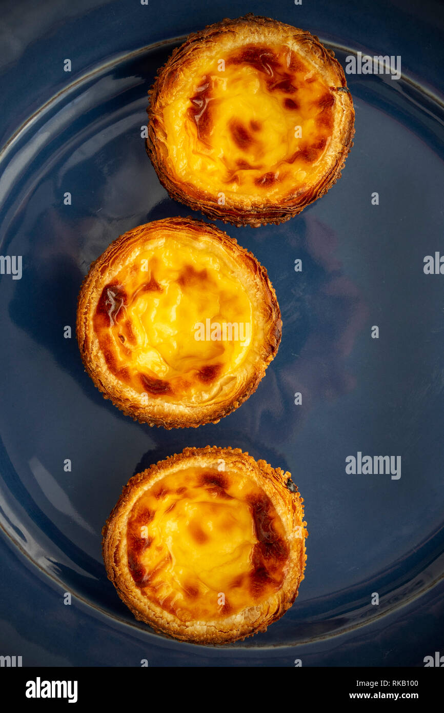 Flach Bild von drei Pastel de Natas (PastÃ© ist de BelÃ©m), auf einem blauen Hintergrund portugiesisches Steingut Teller Pudding Stockfoto