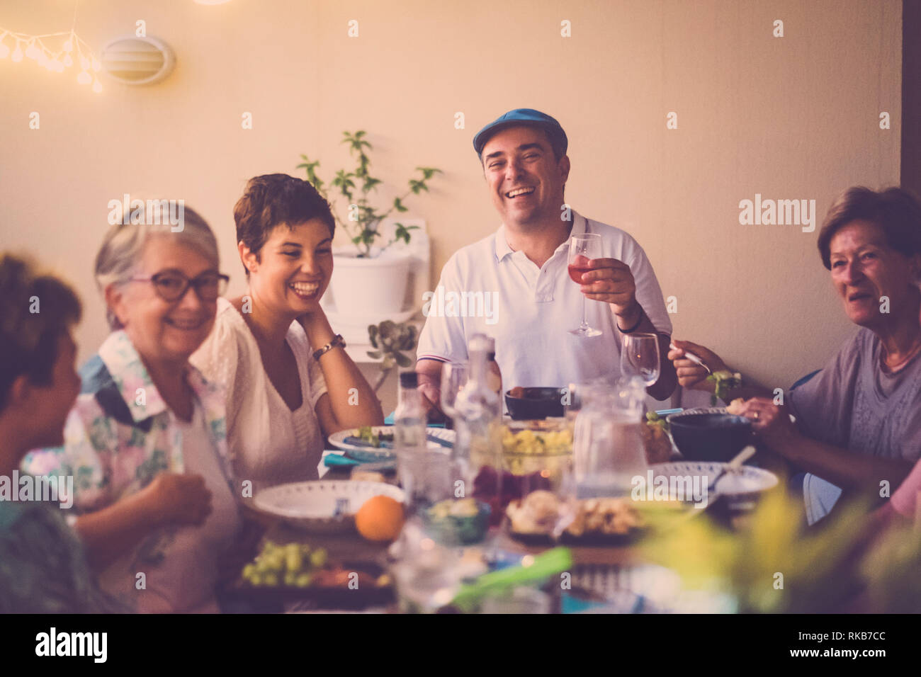 Abendessen mit langen Tisch voller gemischt Essen und Getränke - die Menschen in Freundschaft genießen die Zeit mit Lächeln und Lachen - Fokus auf letzte Mann Lachen Stockfoto