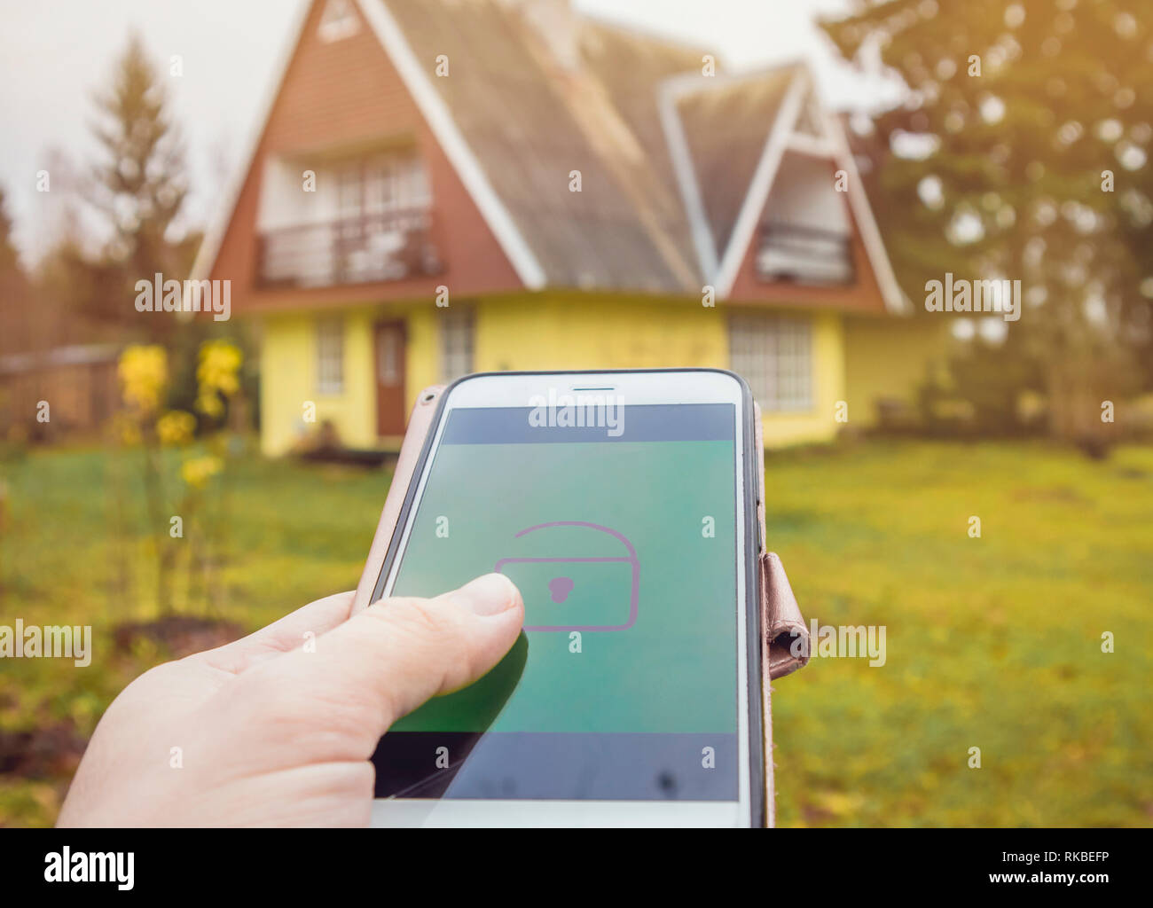 Person Hand Drücken Sie die Verriegelungs-/Entriegelungstaste aus der Distanz auf dem Smartphone App zum Öffnen/Schließen der ländlichen Home Haus Tür. Moderner Lifestyle Technologie Konzept. Stockfoto