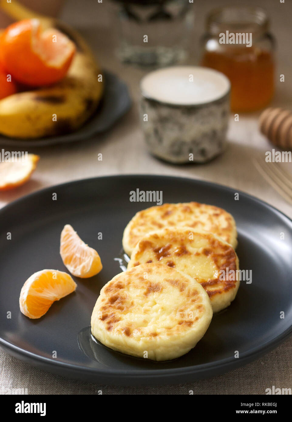 Vegetarisches Frühstück von Quark Pfannkuchen mit Honig, Obst und Kaffee mit Milch. Im rustikalen Stil. Stockfoto