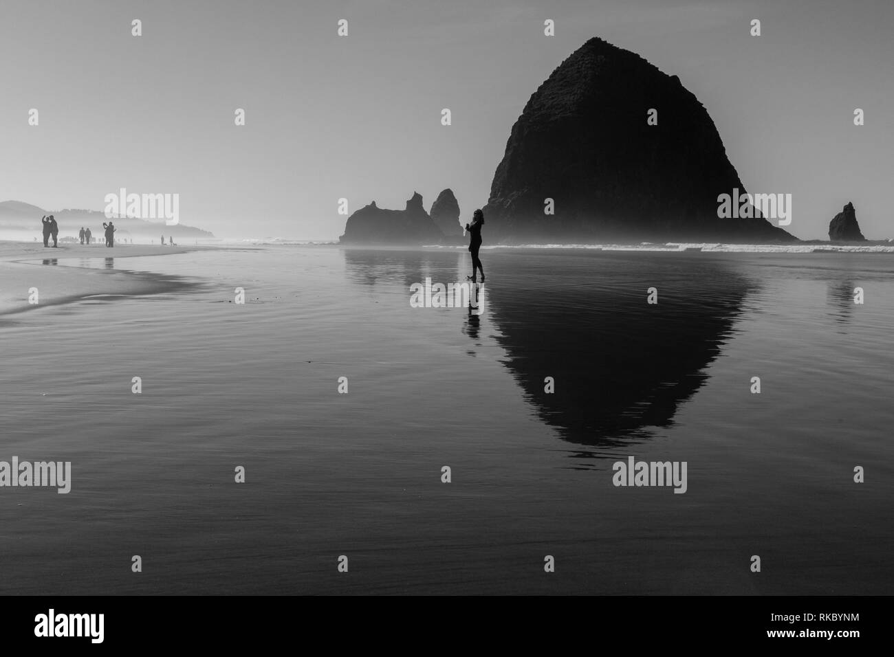 Touristen und Einheimische genießen den Strand mit Haystack Rock im Hintergrund bei Cannon Beach, Oregon, USA. Stockfoto