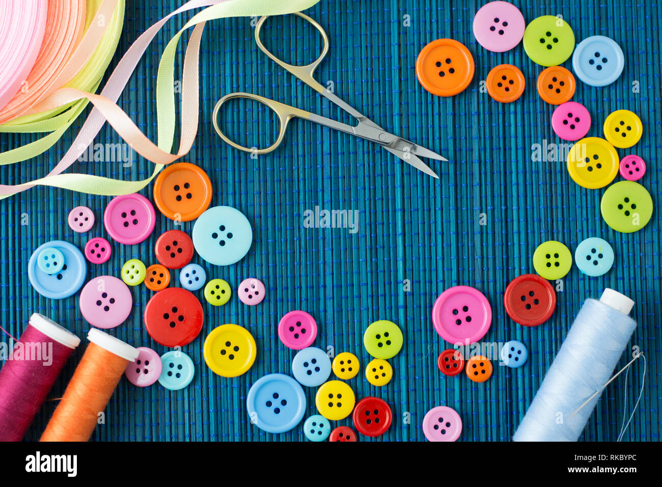 Anpassung der Ausstattung: Viele bunte Buttons, Fäden, Bänder, Scheren und eine Nadel auf ein dunkles Blau Strohmatte-text-Raum Stockfoto