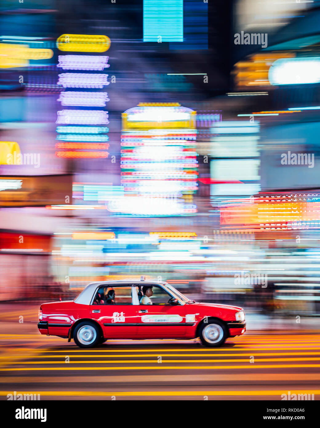 Neonröhren sind lebendig in Hongkong, ein rotes Taxi Geschwindigkeit durch eine Kreuzung in Kowloon, Hong Kong. Taxis sind eine kostengünstige Möglichkeit, zu pendeln. Stockfoto